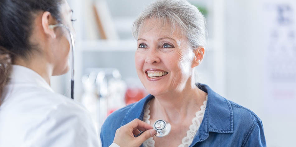 A doctor listens to a woman’s heart with a stethoscope.